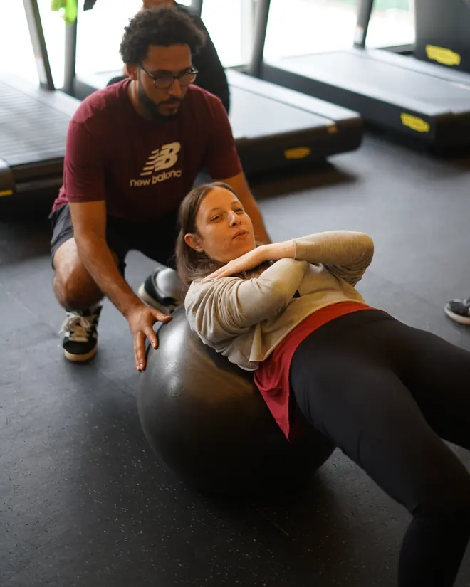 Treinador orientando uma aluna em exercício de abdômen na bola suíça